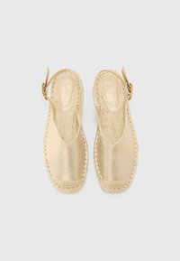 Zlatne espadrile sa slingback dizajnom, tkani jute potplat i glatka, metalik gornja obrada. Ima bočno kopčanje na dugme.
