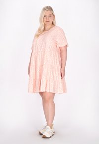 Růžové šaty s krátkým rukávem a bílými tečkami, vrstevnatý design, volný střih a kulatý výstřih, doplněné bílými a béžovými teniskami.