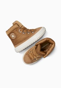 Baskets montantes beiges avec un col rembourré, tige en cuir et textile, semelle en caoutchouc blanche et œillets en argent. Présente un patch avec un logo étoile.