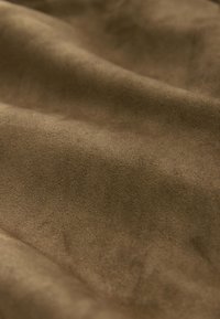 Gros plan d'un tissu en daim brun doux montrant une texture lisse et des plis délicats.