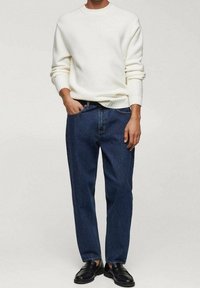Maglione bianco a maglia con colletto tondo, abbinato a jeans di jeans blu scuro. Calzature nere completano l'outfit. Design semplice e casual.