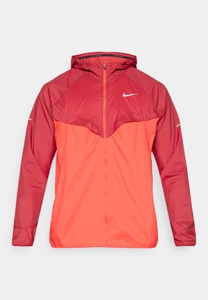 Veste rouge avec capuche, dotée d'une fermeture éclair frontale, d'une section supérieure contrastante en rouge plus foncé, et d'accents de logo blancs sur la poitrine et les manches.