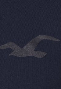 Marinblått tyg med en stor, grå mås grafik. Texturen verkar mjuk och stickad, med en subtil glans på trycket.