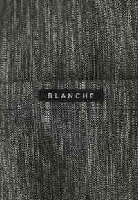 Tecido cinza texturizado com um padrão de denim, apresentando um rótulo preto com a inscrição "BLANCHE" cosido na parte superior.