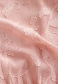 Tissu rose clair avec un motif jacquard floral délicat et une texture douce légèrement froissée.