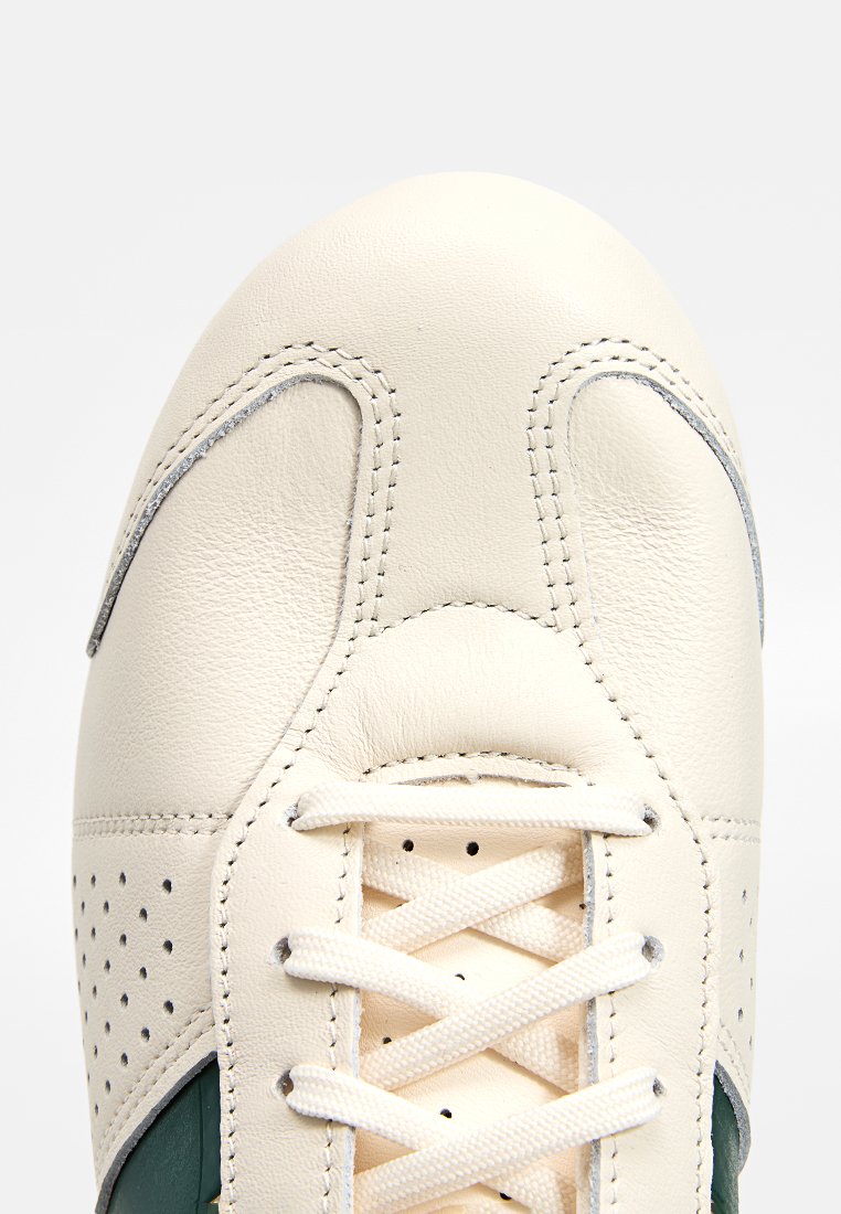 Skórzane sneakersy z kremowym wierzchem, perforowanymi akcentami, zielonymi detalami i płaskim zapięciem na sznurowadła. Posiadają haftowany wzór i gładką teksturę.
