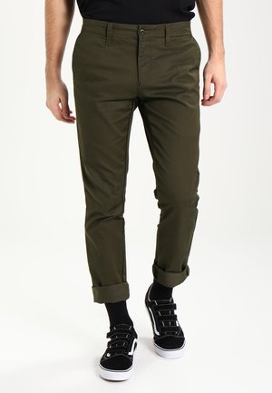Olive green chinos with a slim fit, featuring front pockets and cuffed hems. Paired with black sneakers and crew socks.