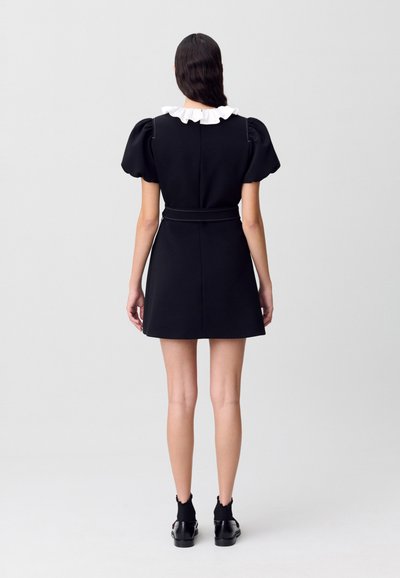 Vestido negro con mangas abullonadas y cuello rizado blanco. Presenta una cintura ajustada y una falda acampanada, confeccionado en un tejido estructurado.