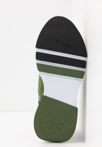 Semelle de chaussure Ted Baker avec sections en caoutchouc noir, blanc et vert et grip texturé, incluant le logo Ted Baker embossé.