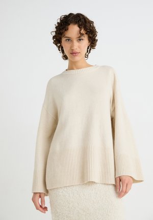 Beige oversized knitted sweater with ribbed hem and wide sleeves, made of soft fabric, featuring a round neckline and textured finish.