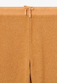 Strickhosen in warmem Orange, mit strukturiertem Stoff und elastischem Bund mit Kordelzug. Goldene Akzente an den Enden des Kordelzugs.