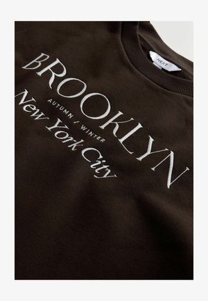Brauner Sweatshirt mit weißem Text: "BROOKLYN HERBST / WINTER New York City", mit Rundhalsausschnitt und weicher Textur.