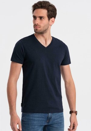 Camiseta azul marino de cuello en V confeccionada en tejido de mezcla de algodón, de manga corta y ajustada de forma relajada. Presenta una etiqueta en el lado izquierdo.