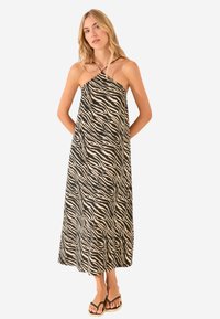 Maxi dress con stampa zebra nera e crema, design a collo halter, tessuto fluido e taglio alla caviglia, abbinato a infradito nere.