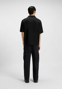 Schwarzes Kurzarmhemd mit Kragen, kombiniert mit schwarzen Cargo-Shorts mit Seitentaschen. Glattes Material mit einem schlichten Design.