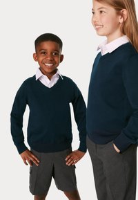 Des pulls en maille bleu marine avec un col en V, portés par-dessus des chemises blanches à col, assortis avec des shorts et des pantalons gris, sur deux enfants.