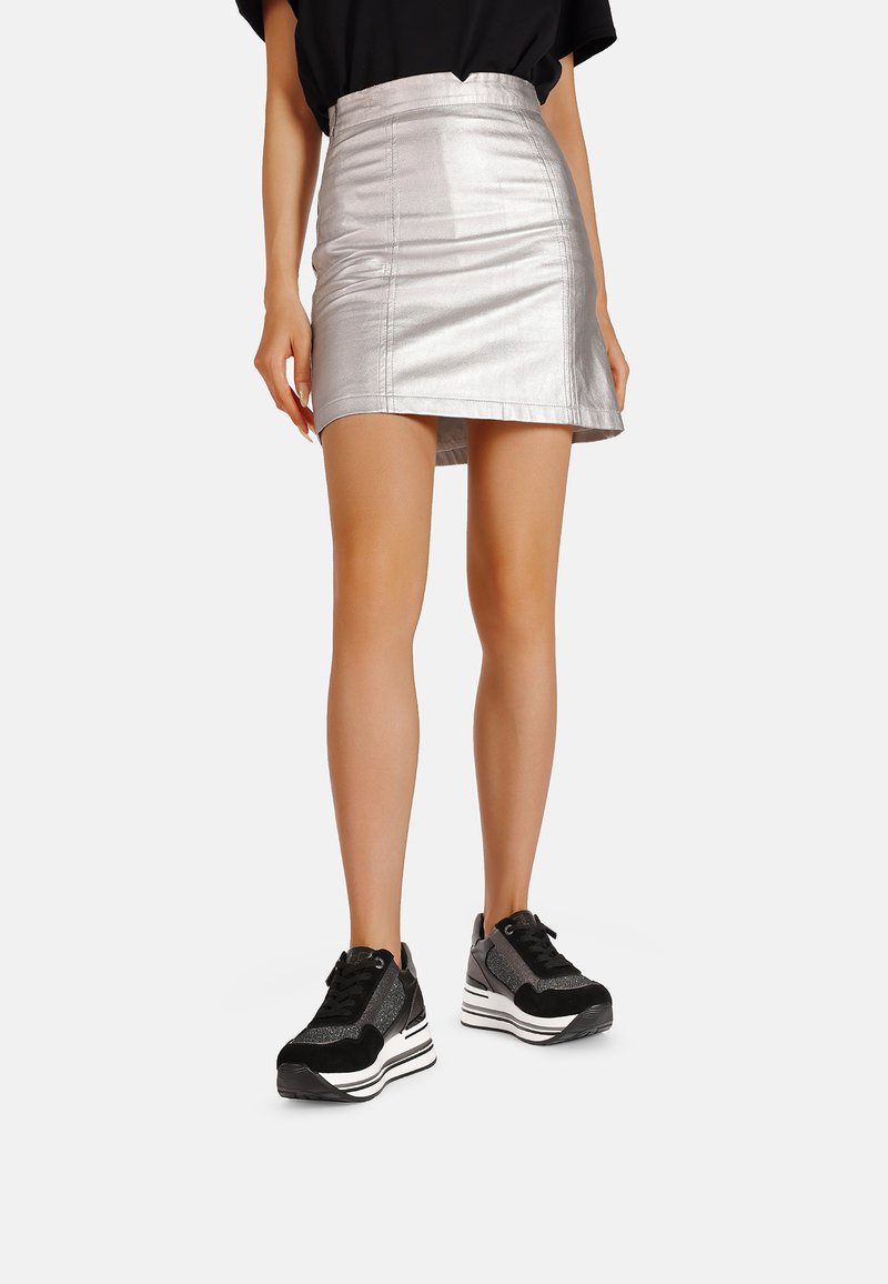 Mini gonna metallica argento con un design aderente, abbinata a sneakers nere massicce con dettagli bianchi e texture.