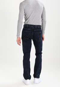 Mörkblå denimjeans med rak passform, med bakfickor och midjeband. Kombineras med en åtsittande grå, ribbad långärmad topp.