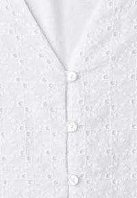 Tissu blanc avec motif brodé floral à œillets présentant de petits boutons ronds en rangée verticale.