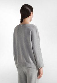 Maglione oversize grigio chiaro con orlo e polsini a coste, texture morbida, maniche larghe e un'etichetta discreta sul retro del collo.