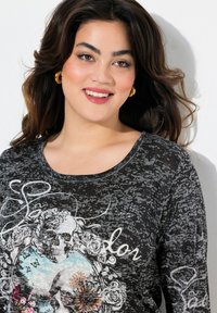 Schwarzes Langarmshirt mit Rundhalsausschnitt, das ein Grafikdesign mit einem Totenkopf und floralen Akzenten zeigt. Weiche Textur mit einem gemusterten Design.