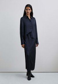 Conjunto de camisa y falda a rayas marineras fabricado en tejido suave; presenta un cuello, cierre de botones en el frente y una cintura con cordón, con mangas largas.