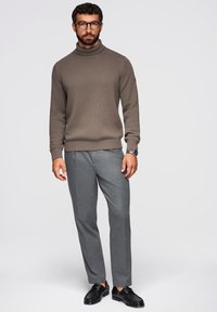 Brązowy sweter z golfem w prążki w zestawieniu z szarymi dopasowanymi spodniami i czarnymi eleganckimi butami. Strój charakteryzuje się swobodnym, ale eleganckim wyglądem.