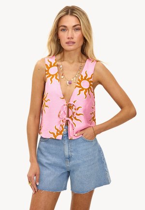 Top sin mangas en color rosa con un escote en V profundo, adornado con patrones de sol marrón. Atado en la cintura, combinado con shorts de mezclilla para un look casual.