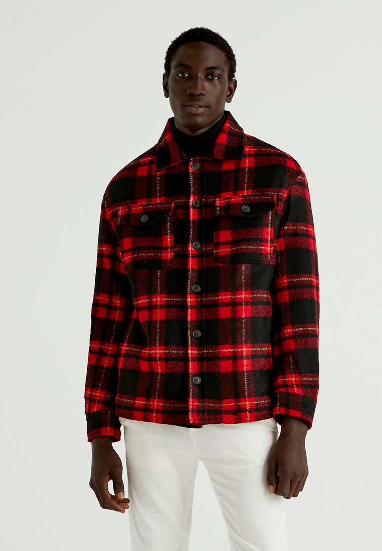 Red and black plaid jacket with a button-up front, two chest pockets, and a collared neckline. Made of textured fabric.