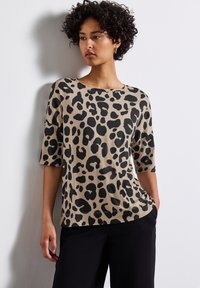 Leopard print top in beige with black spots, featuring a round neck and three-quarter sleeves. Soft fabric with a smooth texture.