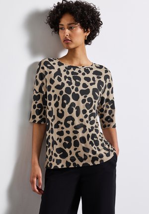 Top in stampa leopardata beige con macchie nere, caratterizzato da un collo tondo e maniche a tre quarti. Tessuto morbido con una texture liscia.
