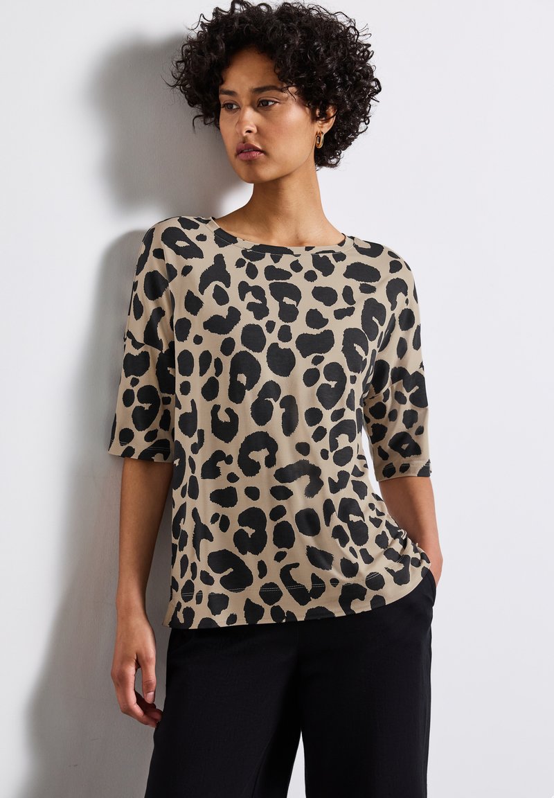 Leopard print top in beige with black spots, featuring a round neck and three-quarter sleeves. Soft fabric with a smooth texture.