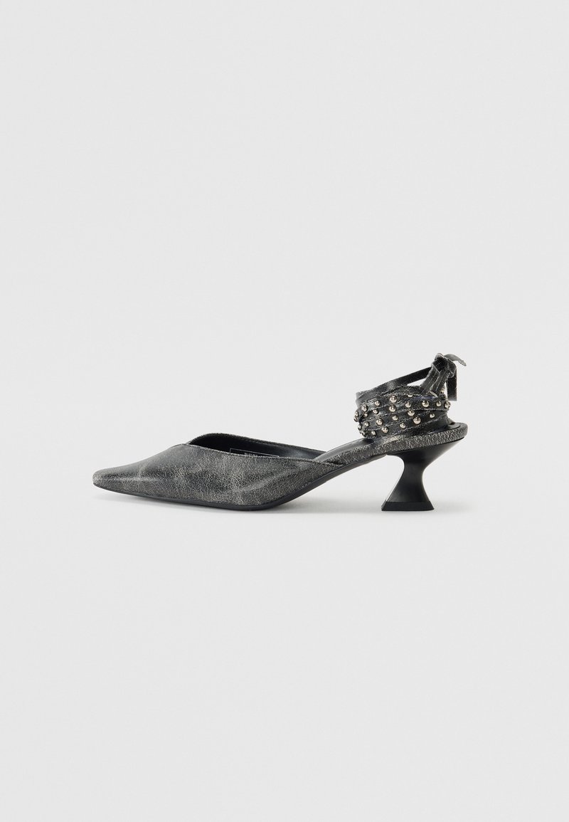 Sandal noir texturé à talon ouvert avec un bout pointu et un talon incurvé. Équipé de clous métalliques sur la bride de cheville pour un détail supplémentaire.