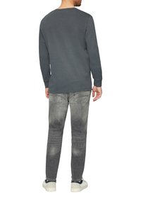 Dunkelgraues Langarmshirt mit Rundhalsausschnitt, kombiniert mit hellgrauen Jeans. Die Schuhe sind weiße Sneakers mit dunklen Akzenten.