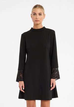 Robe noire à manches longues avec des accents en dentelle aux poignets. Encolure haute, forme fluide en A et texture de tissu lisse.