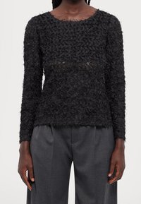 Schwarzes Langarmshirt mit strukturiertem Blumenmuster, transparenten Einsätzen, Rundhalsausschnitt und lockerem Schnitt, kombiniert mit grauen, hoch taillierten Hosen.