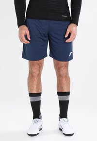 Marineblå sportshorts med afslappet pasform, parret med knæhøje sorte og gråstribede sokker og hvide træningssko. Glat, let materiale.