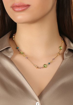 Halskette in Goldoptik mit bunten Perlen in Grün, Blau und Pink, die eine Mischung aus Formen und Größen aufweist, getragen über einem taupefarbenen Satinhemd.