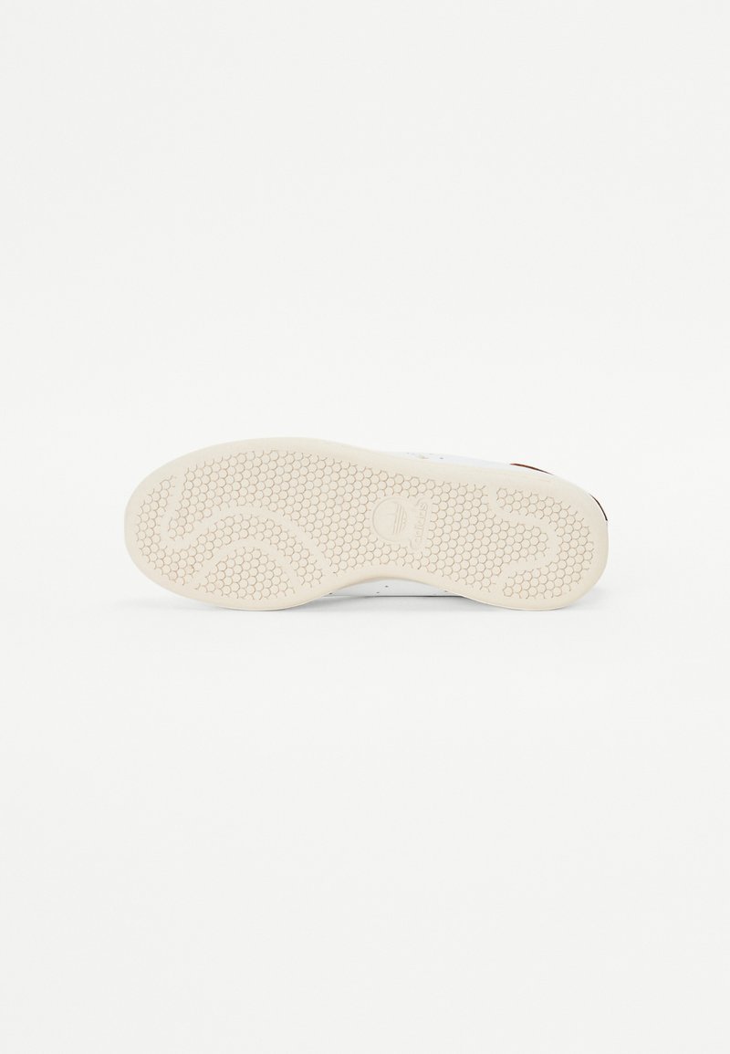 Baskets blanches avec une semelle en caoutchouc texturé, dotée d'un motif en nid d'abeille et d'un petit logo. Les zones visibles sont propres et minimalistes.