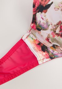 Büstenhalter-Träger mit Blumenmuster, rosa Mesh-Stoff und verstärkten, genähten Nähten auf weißem Hintergrund.