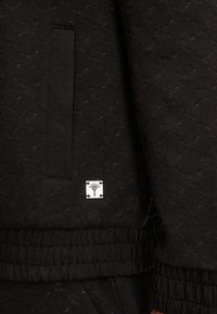 Felpa nera con un motivo testurizzato, polsini a costine e una piccola etichetta logo quadrata bianca. Tessuto morbido con un design versatile.