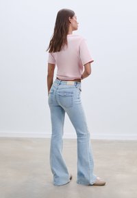 Helle, ausgefallene blaue Jeans mit Taschen, kombiniert mit einem kurzen rosa Oberteil. Die Jeans haben eine strukturierten Oberfläche und ein schlichtes Etikett auf der Rückseite.