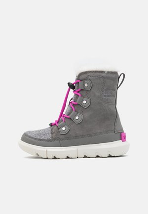 Botte d’hiver grise avec semelle blanche, lacets roses et doublure en polaire, avec œillets métalliques et languette à l’arrière.