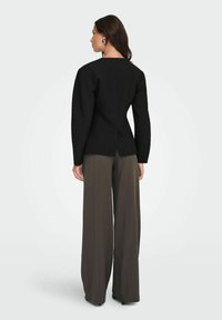 Černý strukturovaný top s dlouhými rukávy a rozparkem vzadu; kombinován s tmavě hnědými kalhotami s vysokým pasem a širokými nohavicemi.