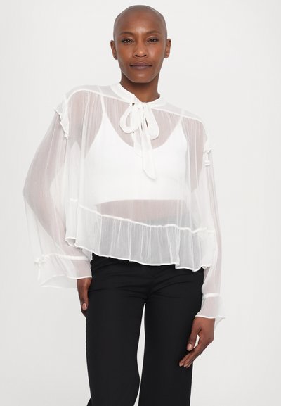Transparante witte blouse met ballonmouwen, gerimpelde zoom en strik halslijn. Gepaard met zwarte, getailleerde broek. Zachte, lichte stof.