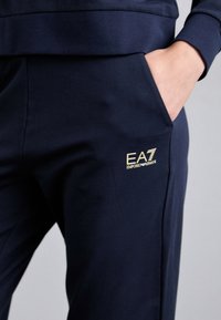 Jūras spēku treniņbikses ar gludu tekstūru, kurām ir sānu kabata un zelta EA7 Emporio Armani logo apakšējā kājas daļā.