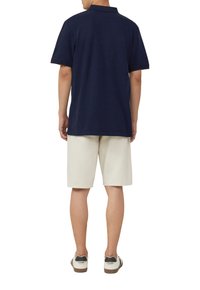Polo bleu marine à manches courtes, associé à un short beige clair. Le polo a un col classique et une coupe décontractée.