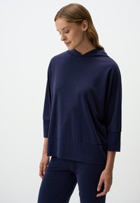 Pullover con cappuccio blu navy, maniche a tre quarti, vestibilità rilassata e texture liscia. Presenta una cucitura all'altezza della vita.