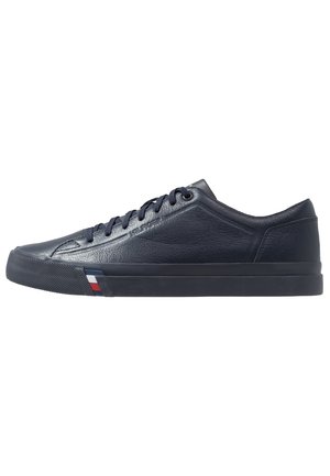 Dark blue low-top leather sneaker with dark laces, textured rubber sole, and a small red, white, and blue stripe detail near the front.