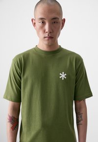 Oliven grøn bomulds t-shirt med rund hals, korte ærmer og et hvidt stjerne-logo på venstre bryst. Glat tekstur, afslappet pasform.